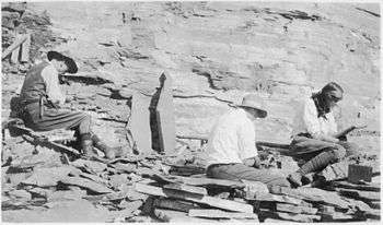 Photo of two men and a woman digging among rocks.