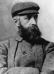 A portrait photograph of a bearded man in a plain hat and jacket