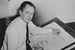 Black-and-white photograph of a man seated at a drawing table and drawing a cartoon
