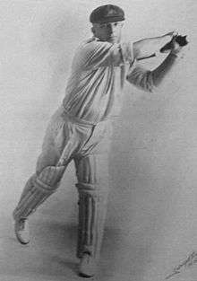 Studio portrait against a white background of a stocky cricketer in white shirt and trousers with rolled up sleeves, cricket pads, baggy green cap with Australia coat of arms, wearing gloves and holding a bat and swinging it horizontally to his left. He is a right-hander and his leading left leg is straight but his right leg is bent with only the toes on the ground.
