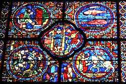 Part of a large window. It is divided into four circular panels with a quatrefoil (or four-lobed section) between them and an arched segment beneath. To the lower right, a knight, Sagittarius, is being welcomed home. At the centre a man empties a water pot, symbolising Aquarius and a two-faced figure symbolises New Year. To the upper right, are the two fish of Pisces. The other sections show each month's activities: grapevine pruning, bell-ringing and sitting by the fire.