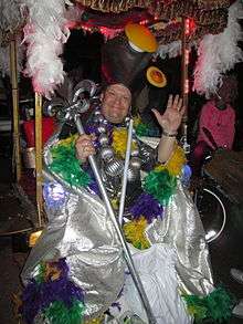 Andy Richter smiling and waving wearing an elaborate and colorful costume