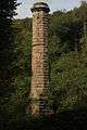 A large six sided chimney made from cut brown stone, surrounded by woodland.