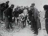 Black and white image of man bending over his bicycle while several other men are watching.