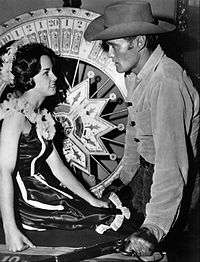 Lucas McCain looking at woman sitting in front of roulette wheel.
