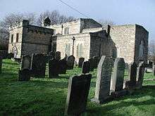 In the foreground are a number of graves marked by head-stones. Behind these is a small stone church building.