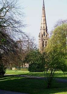 The tall spire of a church seen through parkland