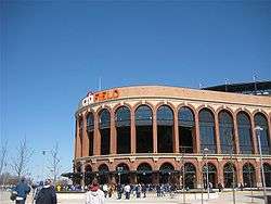 The exterior of a baseball stadium, which has a round brown entrance area with a white and orange "citiFIELD" on top.