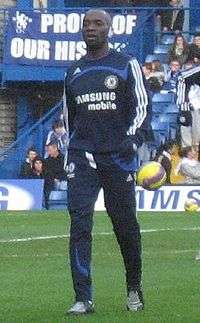 A dark-skinned man wearing a sequential black jogging suit with blue lining.