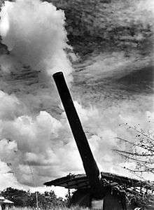 A large calibre gun fires, creating a cloud of smoke