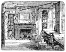 A monochrome illustration of a ramshackle room. Windows allow light to stream in, from the right of the image. Plaster is missing from the ceiling. A large fireplace dominates the far wall, and is surrounded by various cupboards and containers. The floor appears to be formed from planks of wood.