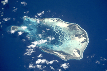 An overhead photograph showing the same atoll with its large lagoon reaching into the island's interior.