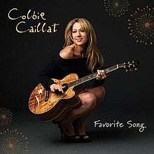 Colbie Caillat crouching, smiling and playing a guitar.