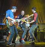 A photo of Coldplay, with three members playing various guitars.
