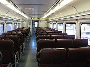 The inside of a train car during daylight, consisting of an aisle and seats on both sides of the aisle.