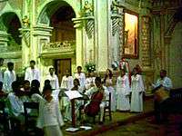 A choir and musicians dressed in white robes inside a church.