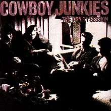 A grainy black-and-white photo of Cowboy Junkies sitting in a semicircle, with a rust-colored logo