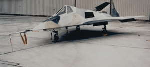 Small jet aircraft with angled surfaces in hangar. It is painted in a disruptive scheme to confused casual onlookers.