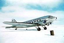 Right side view of a silver Douglas DC-3 aircraft parked on snow-covered ground.