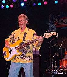 Dunn on stage playing bass guitar wearing a yellow Hawaiian shirt