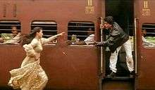A woman in a dress runs to catch a train while a man is waiting with his hand out to help her
