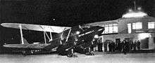 Biplane at terminal at night, with people in background