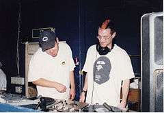 Two men stand behind a set of turntables.