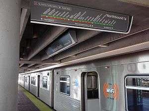 A metro train sits beside a station platform with its doors open.  A map of the metro system hangs from the roof of the station.