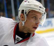 A head shot of a Caucasian hockey player wearing a white helmet with a visor and a white jersey