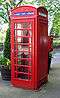 A telephone kiosk painted bright red with a post box and flowers tubs behind.