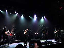 The members of a band perform a song under multi-colored stage lights