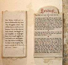 Two stone tablets of similar height set on a plain wall, both with black writing in an elaborate hand.  That on the right also has the title "Exodus" in larger red writing, and several words are picked out in red.
