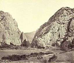 A 19th-century monochrome photograph of a rocky river canyon, with sharp high cliffs in the background.