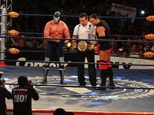 El Texano Jr. and Blue Demon Jr. holding the AAA Mega Championship belt in a wrestling ring