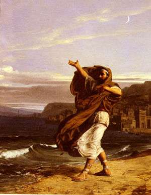  Man in robes with long brown hair against a background of waves reaching the shore