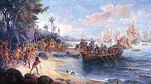 A painting depicting a boat containing armored men being rowed from ships on the horizon onto a shoreline crowded with people in loincloths, while in the background a native kneels before a small group of European men with a large white banner bearing a black cross