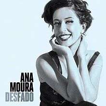 Light-blue toned picture of a smiley woman. She looks at the camera as she has her hands grabbing her neck. She has short black hair, and wears a dress of the same colour. To her right the text "Ana Moura" is written in black capital letters, and below it "Desfado", written in greyish tones.