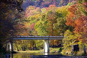 Red, green and orange fall foliage surrounds a small bridge spanning a quiet, rocky Lee Creek