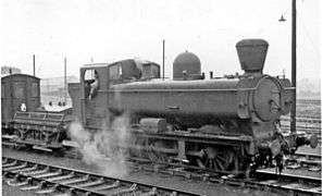 A pannier tank locomotive with a conical chimney is pulling a shunter's wagon and guards van.