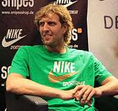 Dirk Nowitzki, seated, wearing a green Nike shirt
