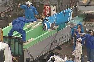 A dolphin in a sling being lowered by staff into one of two dolphin tubs on back of a truck