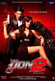 A poster that features two people is shown. A man wearing a tuxedo, looking angry, is sitting on the edge of a throne made of rocks. A female, wearing a black gown and holding a gun in her right hand, is sitting between his parted legs.