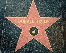 A red five-pointed star surrounded by a brass bezel set in black sidewalk. The words "DONALD TRUMP", and the symbol of a television with antennae, are set into the star in bronze.