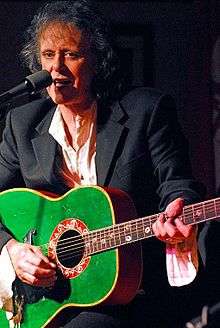 A man playing a green guitar and singing.