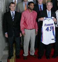 Florida Gators men's basketball coach Billy Donovan, 42 year-old white man shown in navy blue blazer and tie, and his 2007 NCAA championship team, with former Florida Gator Walter Hodge and  U.S. President George W. Bush holding Florida Gators jersey "43," at the White House.