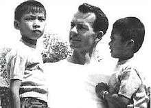 Black and white photograph of Tom Dooley. A white adult man holding two children of Asian descent in his arms.