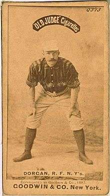 A baseball player standing facing the camera with his hands resting on his knees