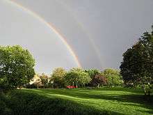 double rainbow over green in bright sunshine with large tree on both left and right of image