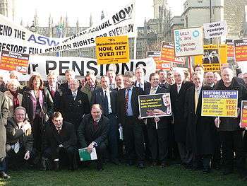 A group of people holding placards standing in front of the Palace of Westminster