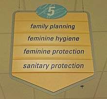 A yellow sign with a pointed bottom. At the top is the number 5 in an oval with a blue background. Below it are the words "family planning", "feminine hygiene", "feminine protection" and "sanitary protection"